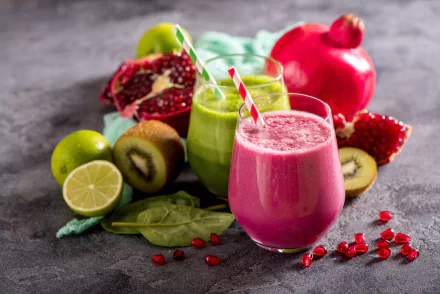 A vibrant 4K Ultra HD still life of two glasses of fresh fruit smoothies—one pink, one green—surrounded by kiwi, lime, spinach, and pomegranate on a textured surface.