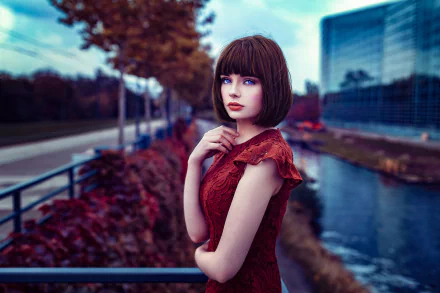 HD desktop wallpaper of French model Marie Grippon with blue eyes and brunette hair, wearing red lipstick and a matching dress by a river in an urban setting.