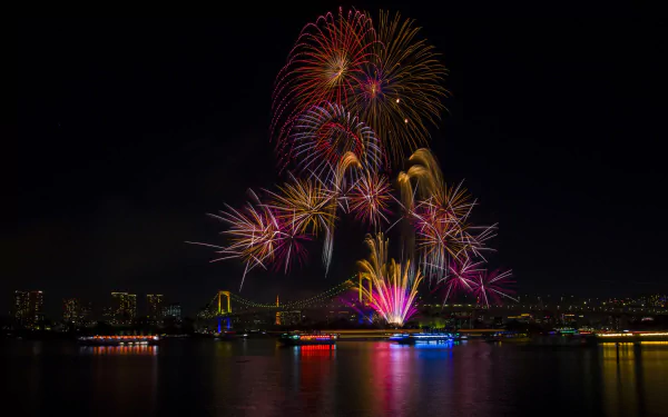 Night photography of Tokyo's Rainbow Bridge in Japan lit over water with colorful fireworks bursting above, reflections on the bay — HD PC desktop wallpaper background.