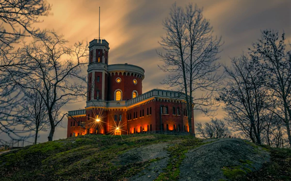 Kastellholmen Castle in Sweden illuminated at dusk, set against a dramatic sky with bare trees surrounding the historic man-made structure.