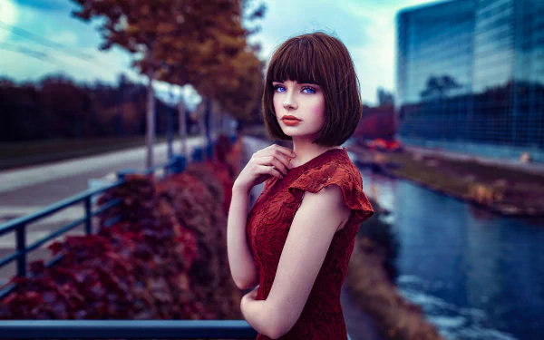 HD desktop wallpaper of French model Marie Grippon with blue eyes and brunette hair, wearing red lipstick and a matching dress by a river in an urban setting.