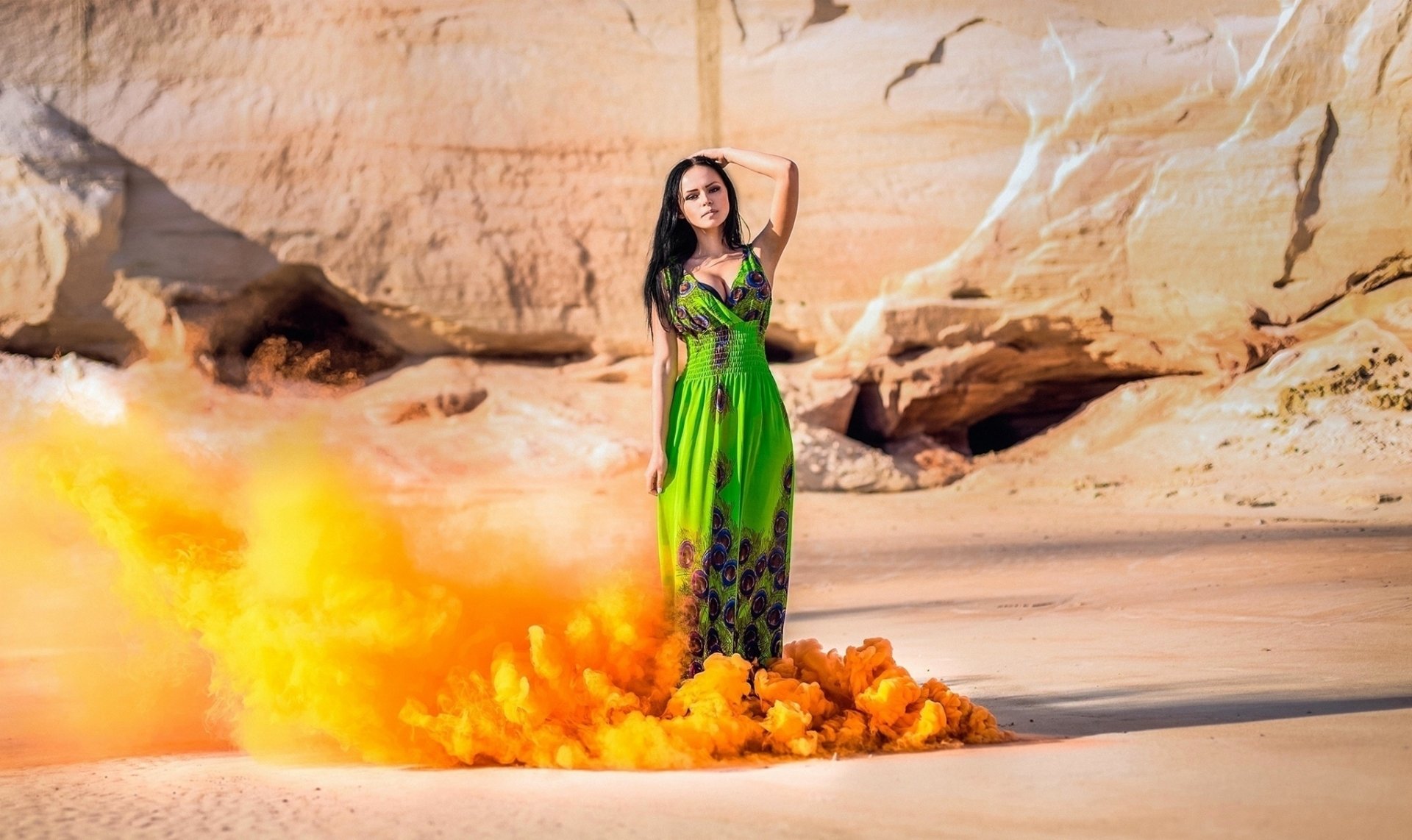 A black-haired woman in a green dress stands confidently on a sandy desert background with orange smoke swirling around her, captured in HD.