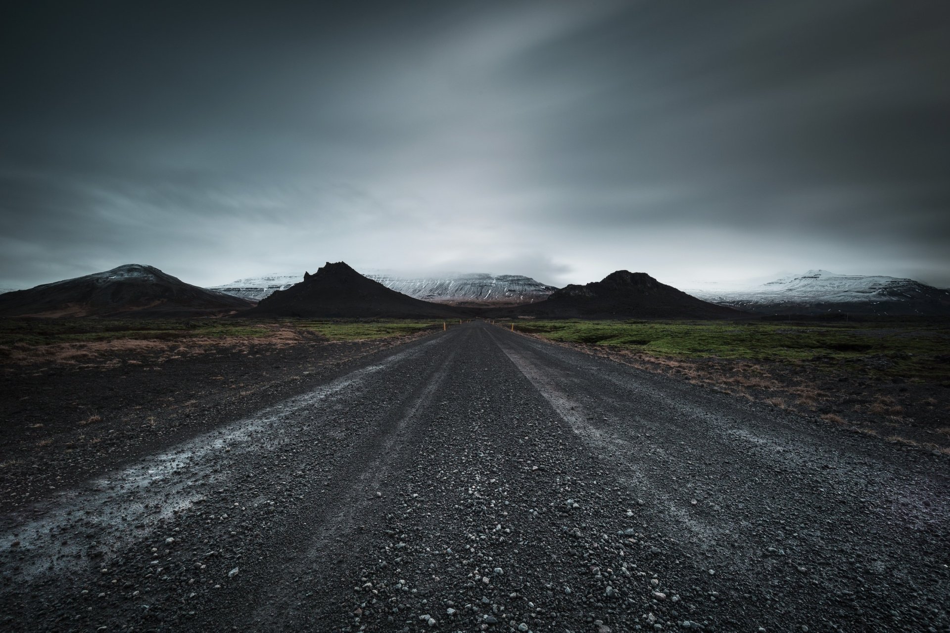 HD desktop wallpaper showing a dirt road leading through a mountainous landscape under a moody, overcast sky surrounded by nature.