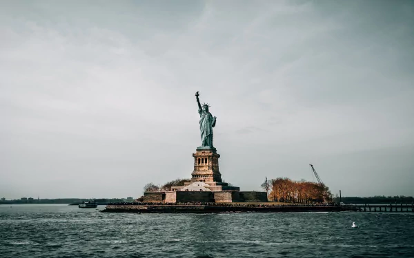 HD desktop wallpaper of the man-made Statue of Liberty in the USA, standing tall against a cloudy sky with water in the foreground.