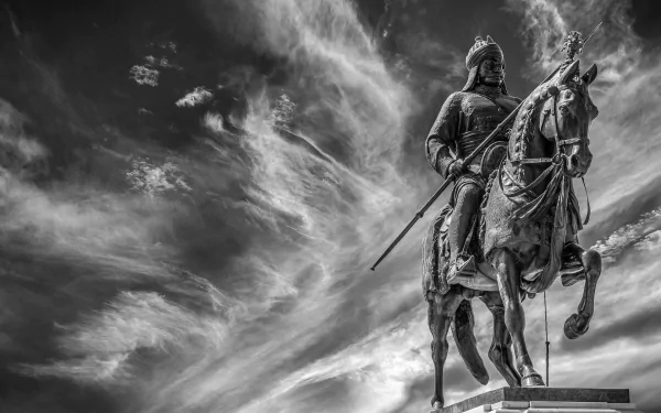 Black and white HD desktop wallpaper of a warrior statue on horseback, set against a dramatic cloud-filled sky, serving as a striking memorial.