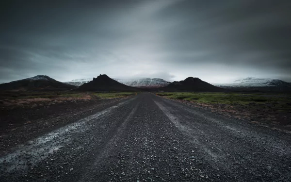 HD desktop wallpaper showing a dirt road leading through a mountainous landscape under a moody, overcast sky surrounded by nature.