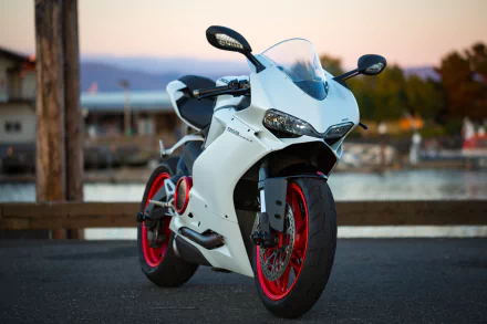 4K Ultra HD desktop wallpaper featuring a sleek white Ducati motorcycle parked by a waterfront at sunset.