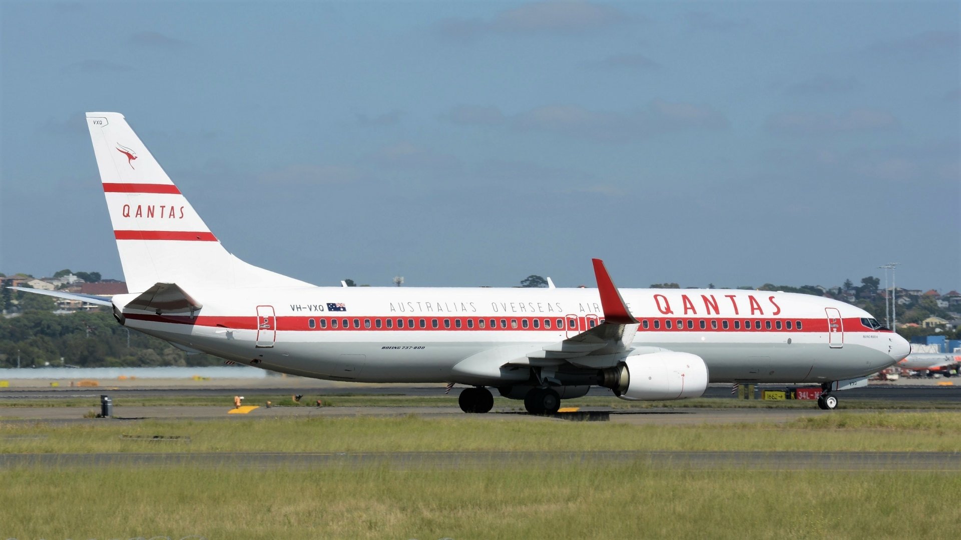 HD desktop wallpaper of a Qantas Boeing 737 passenger plane on the runway, showcasing the aircraft and vehicle against a clear sky background.