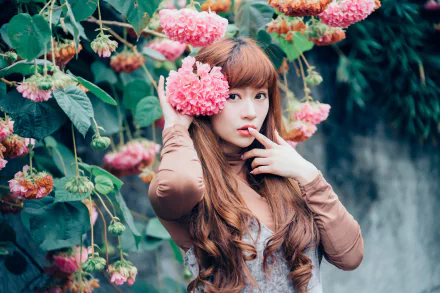 HD desktop wallpaper of an Asian brunette woman with long hair, wearing lipstick, posing among vibrant pink flower clusters in a lush garden setting.