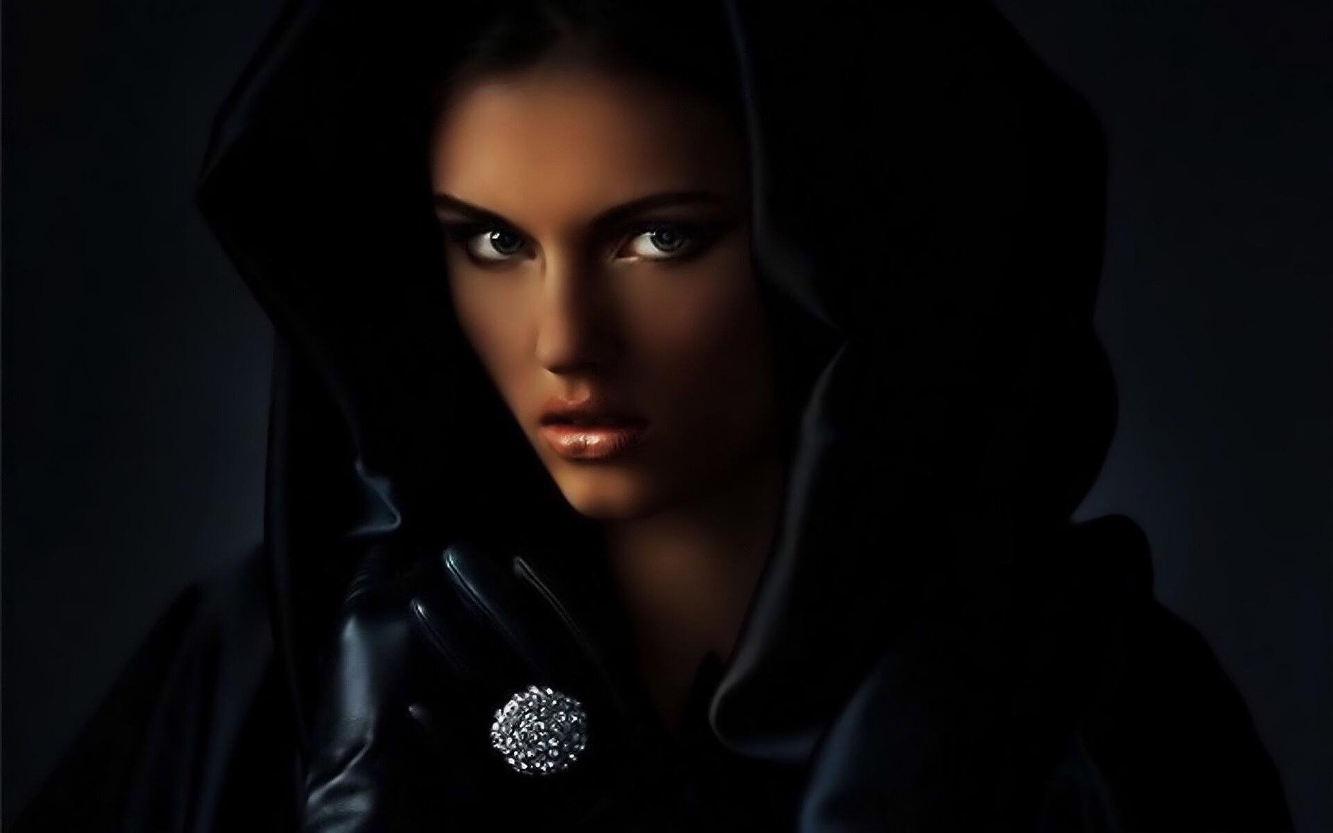 A striking HD desktop wallpaper featuring a woman in a dark hood, exuding a mysterious allure with intense eyes and elegant gloves, set against a dramatic background.
