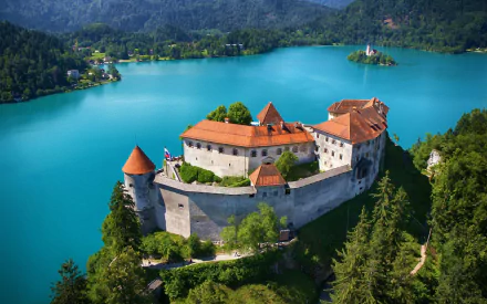 A breathtaking HD desktop wallpaper featuring Bled Castle in Slovenia, perched on a cliff overlooking turquoise Lake Bled, surrounded by lush green forests and mountains.