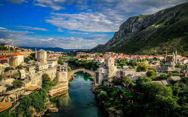 A stunning HD desktop wallpaper of Mostar, Bosnia and Herzegovina, showcasing a historic bridge spanning a river, surrounded by the city's architecture and lush green mountains.