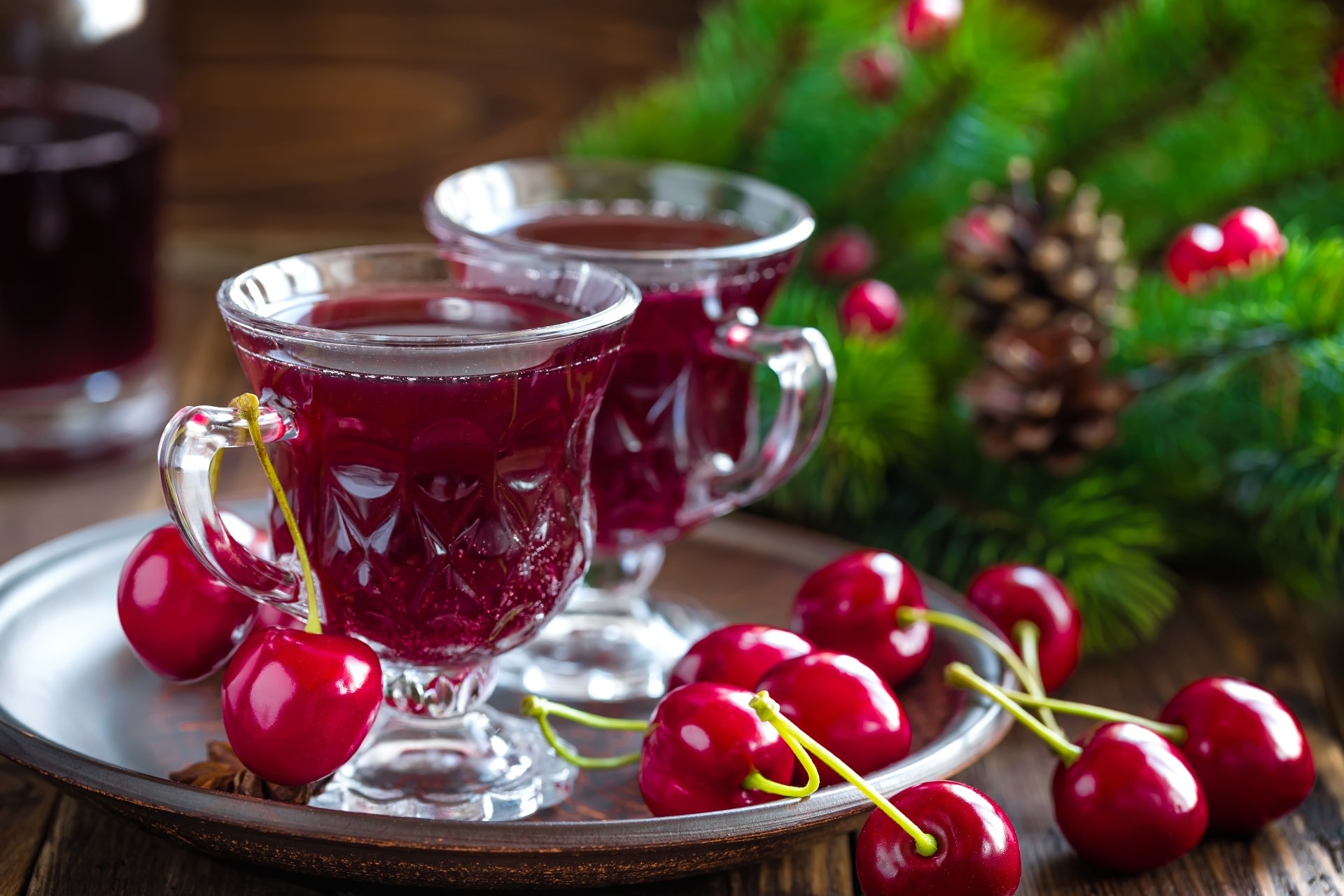 8K Ultra HD PC desktop wallpaper featuring fresh cherries and two glass cups filled with cherry drink, set against a festive green background with pine cones.