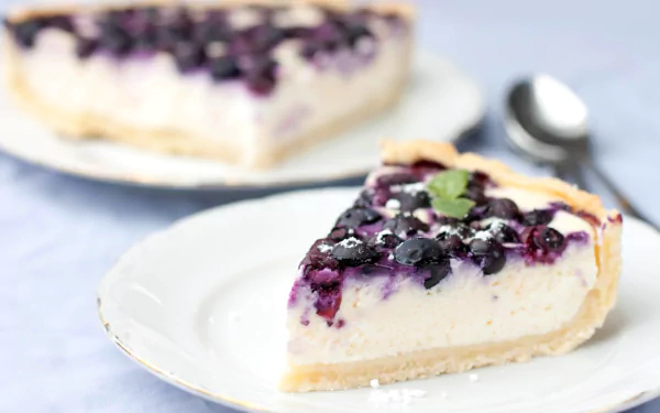 A close-up of a blueberry cheesecake slice on a white plate with another slice blurred in the background, captured in HD for a desktop wallpaper.