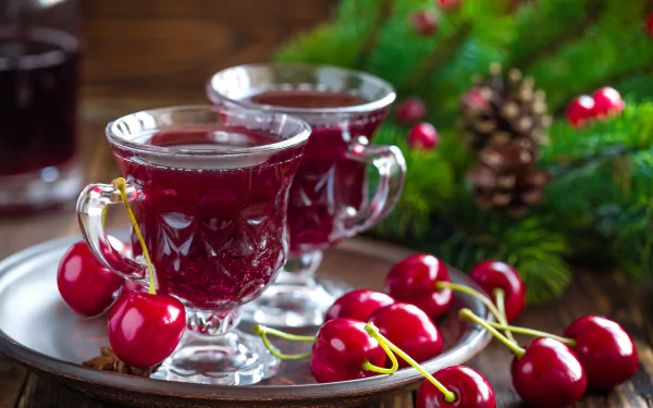 8K Ultra HD PC desktop wallpaper featuring fresh cherries and two glass cups filled with cherry drink, set against a festive green background with pine cones.