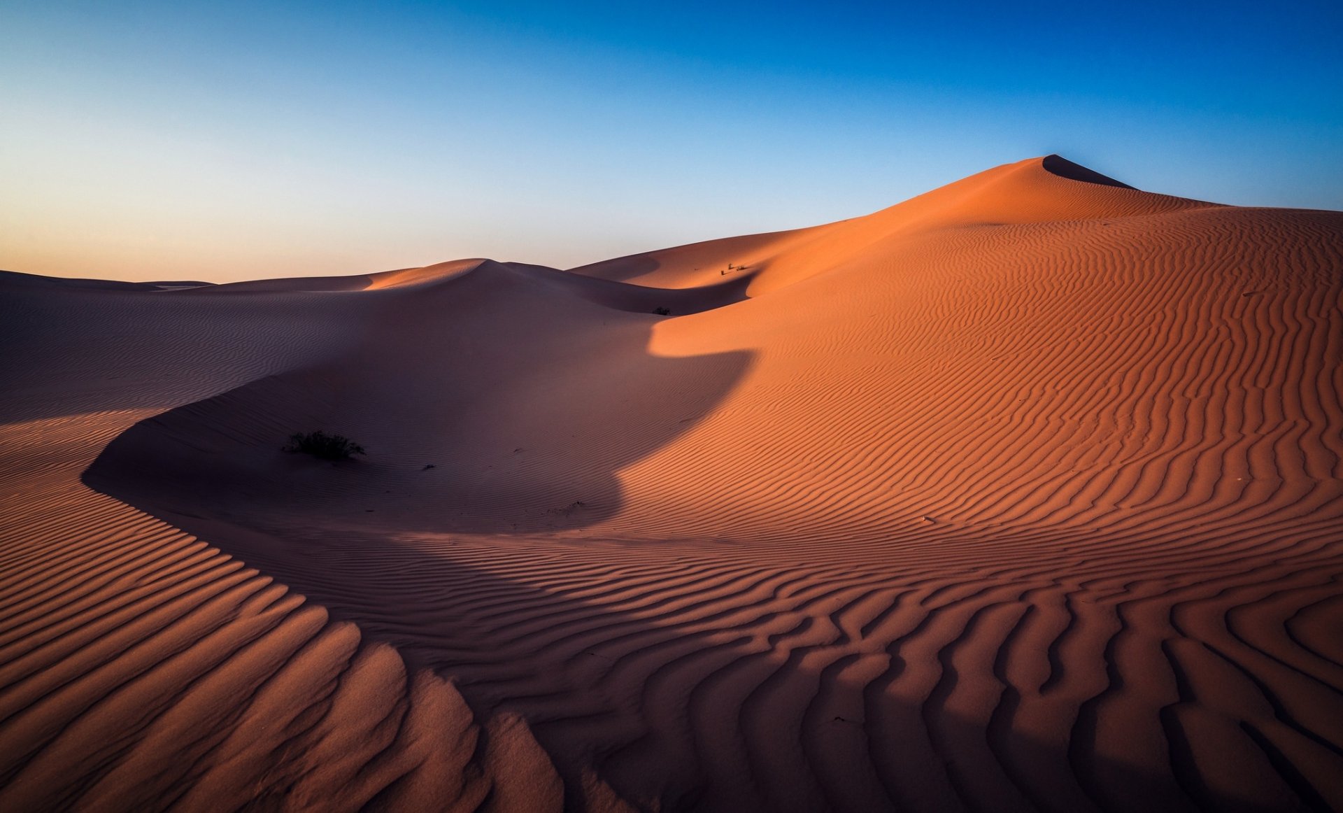 HD PC desktop wallpaper featuring a serene desert landscape with golden sand dunes under a clear blue sky at sunset.