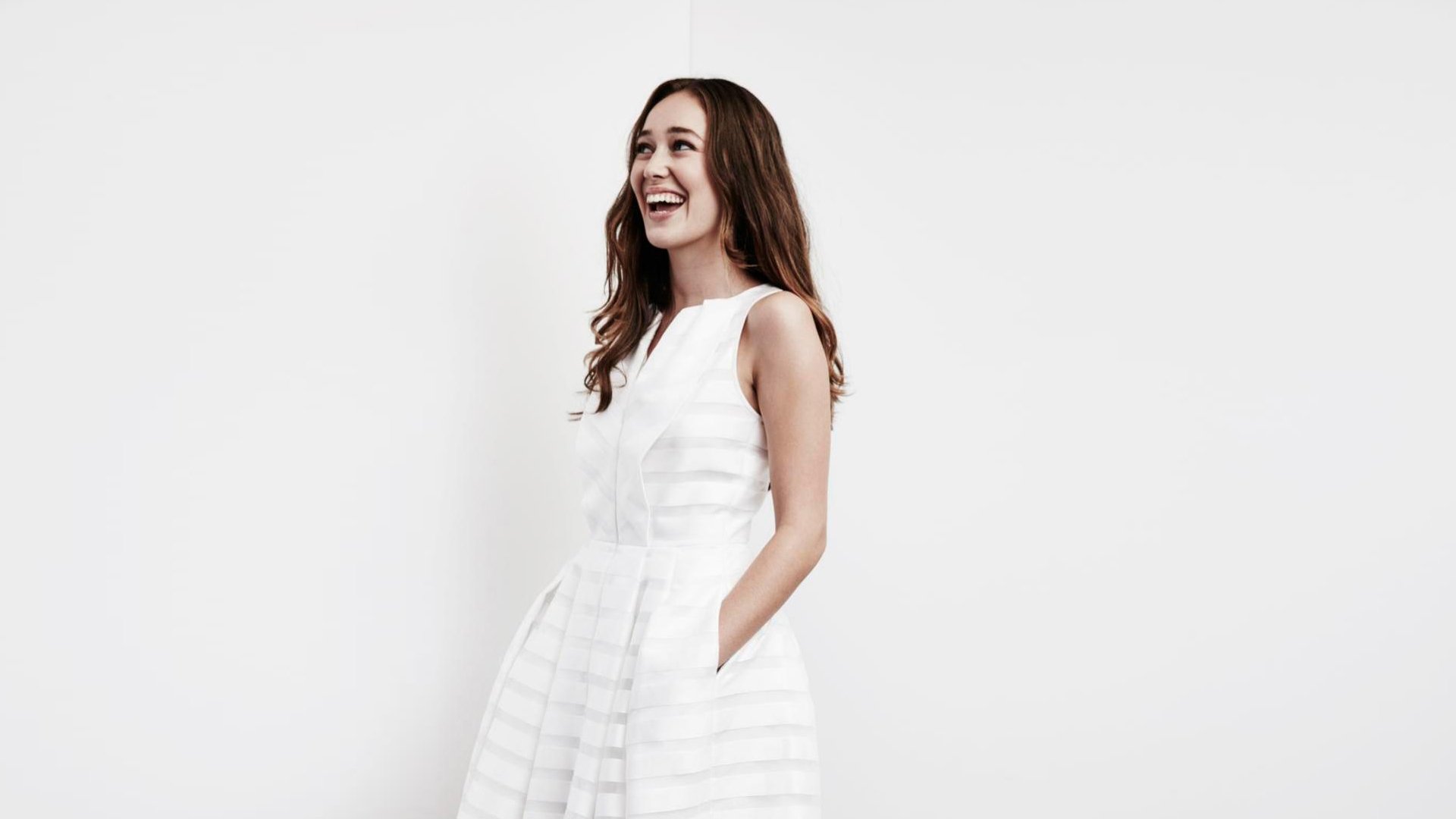 Smiling woman in a white sleeveless dress with hands in pockets against a plain white background — minimalist HD desktop wallpaper.