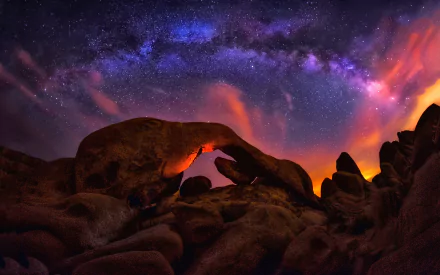 Stunning HD desktop wallpaper of Joshua Tree National Park featuring a vibrant Milky Way arching over rugged rock formations under a starry night sky.