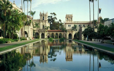 Balboa Park's man-made pond reflects historic castle-style architecture amid lush palm trees, captured in a vibrant HD desktop wallpaper.