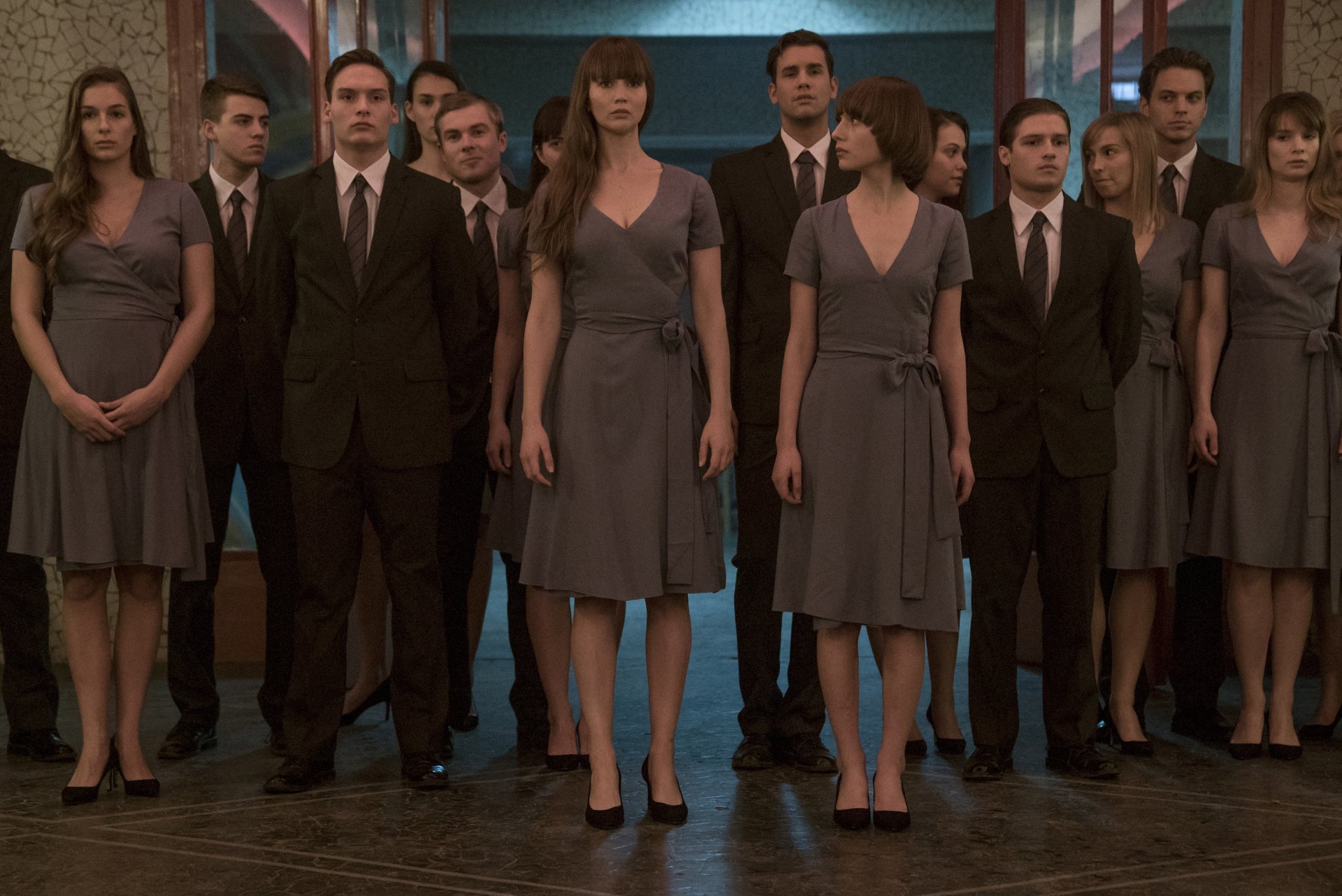 HD wallpaper of a scene from Red Sparrow featuring a group of people in formal attire, standing in a dimly lit room.