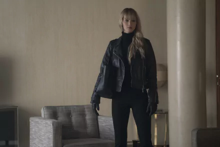 HD wallpaper featuring a character from Red Sparrow, portrayed by Jennifer Lawrence, standing confidently in a dimly lit room.
