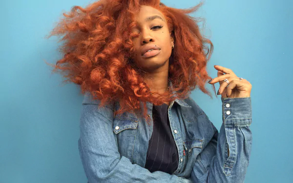 HD desktop wallpaper featuring SZA with vibrant red hair and denim attire against a blue background.