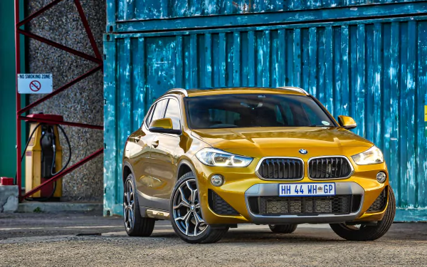 Yellow BMW X2 SUV parked in front of a weathered blue industrial door — 4K Ultra HD PC desktop wallpaper featuring a compact BMW vehicle.