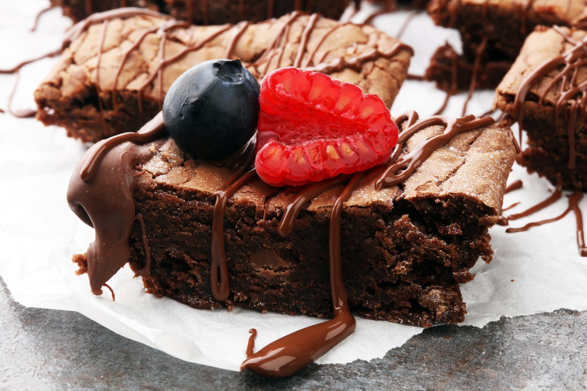 Close-up of a rich chocolate pastry cake drizzled with chocolate sauce, topped with a fresh raspberry and blueberry, captured in 8K Ultra HD for a PC desktop background.