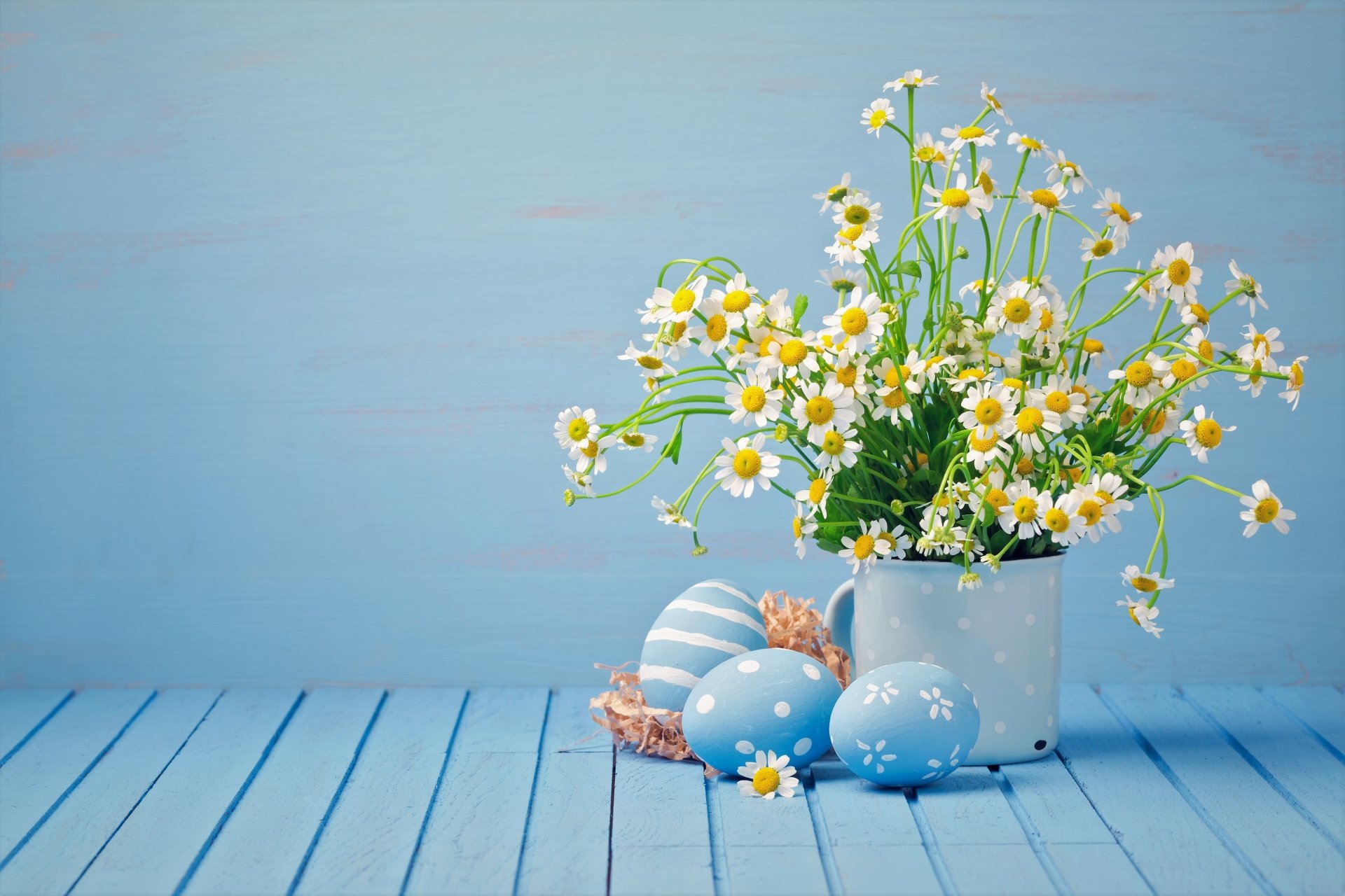 A 4K Ultra HD desktop wallpaper featuring white camomile flowers in a white pot alongside pastel Easter eggs on a light blue wooden surface.