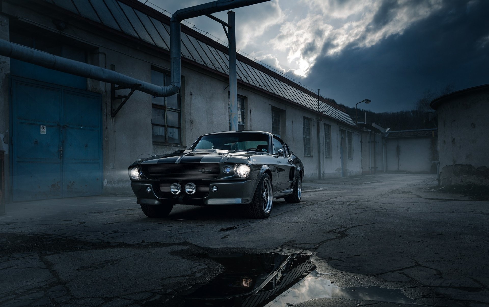 HD desktop wallpaper featuring a sleek Ford Mustang Shelby GT500 muscle car parked in an industrial setting under a dramatic, cloudy sky.