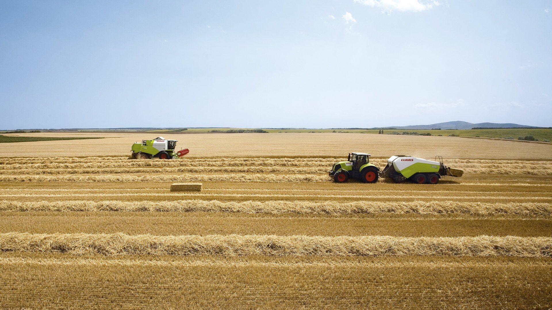 HD PC desktop wallpaper showing a vast farm with two tractors working side by side on harvested fields under a clear sky.