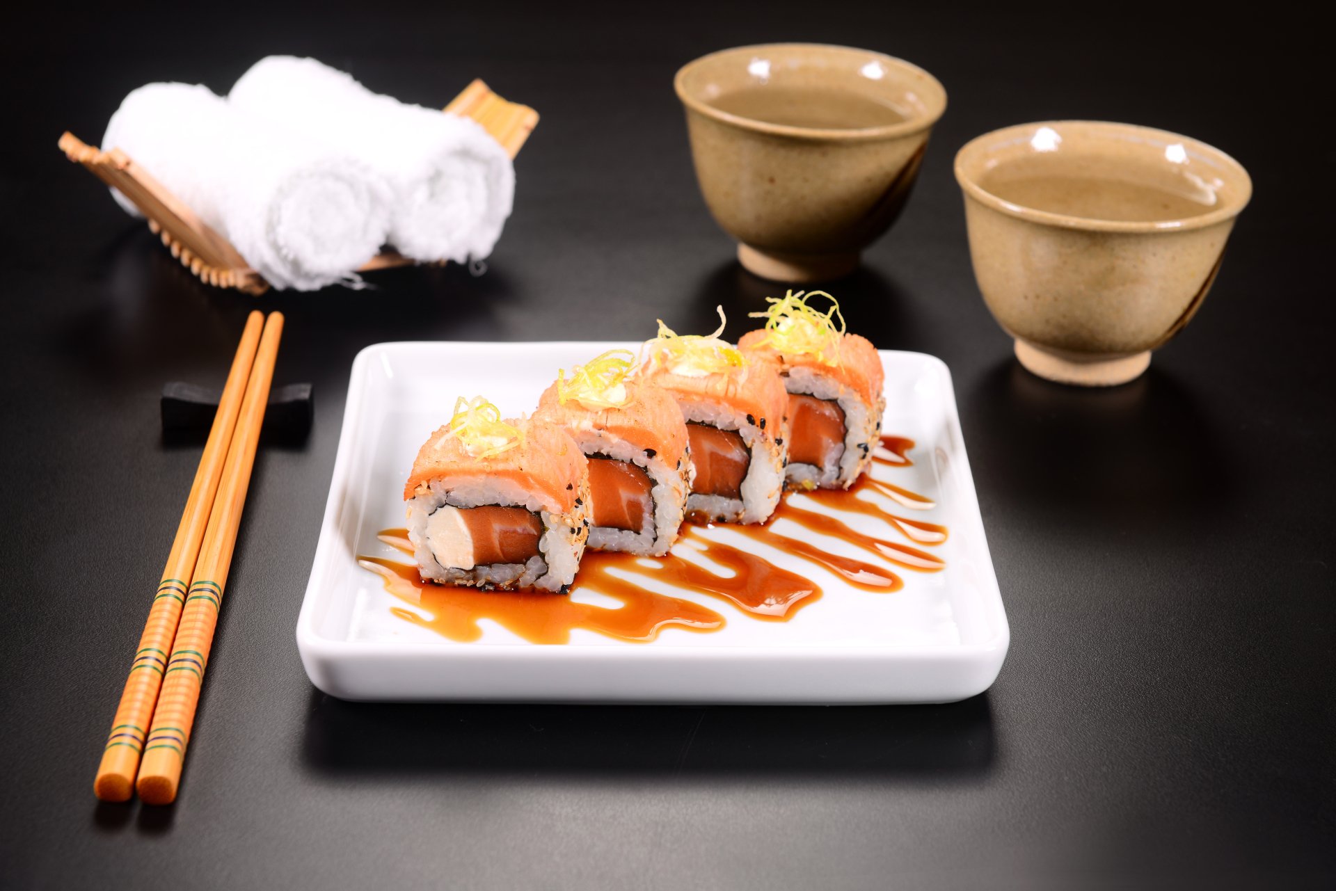 5K Ultra HD PC desktop wallpaper — still-life sushi: plated seafood rolls with sauce and lemon zest, chopsticks and tea cups on a black surface.