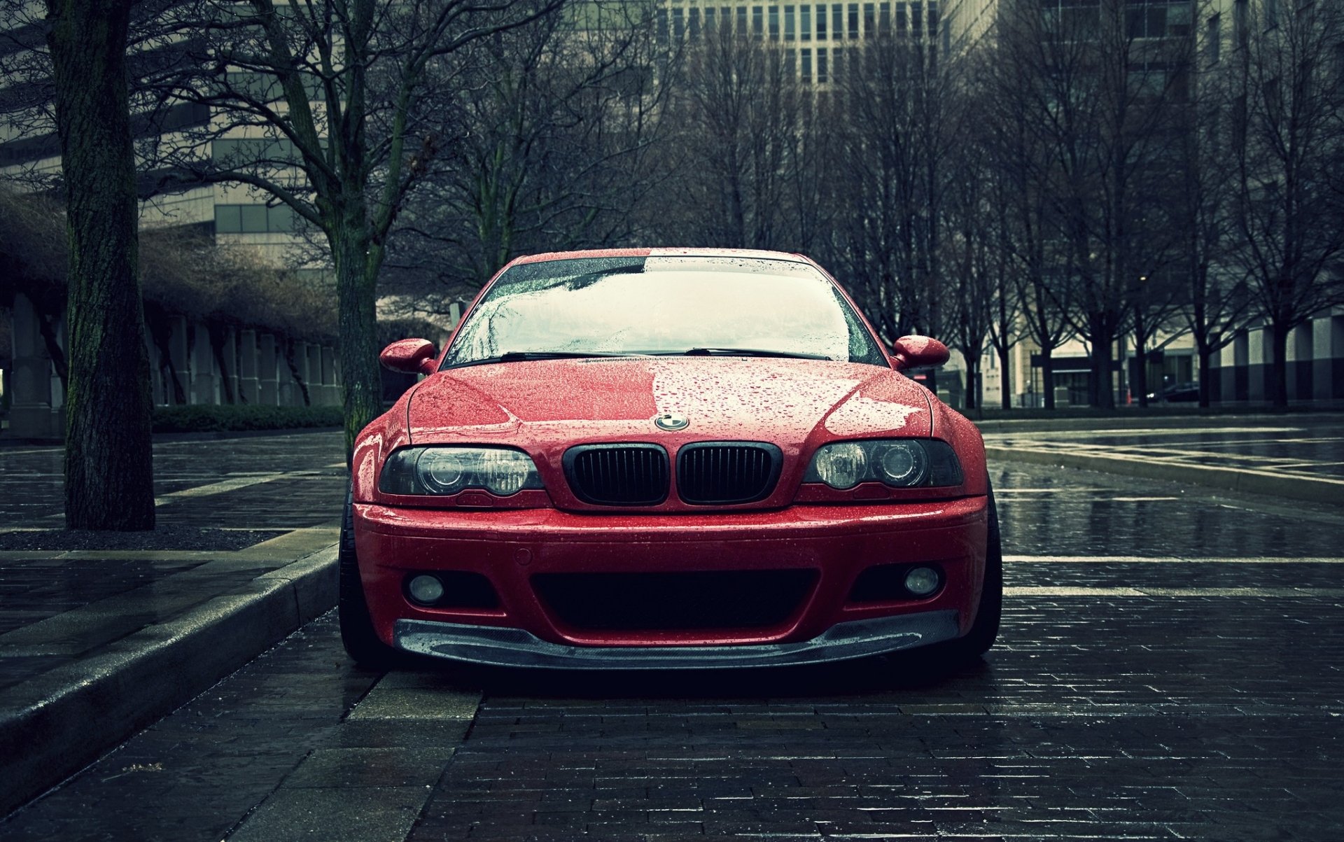 HD desktop wallpaper featuring a red BMW 3 Series car parked on a wet urban street with leafless trees and buildings in the background.