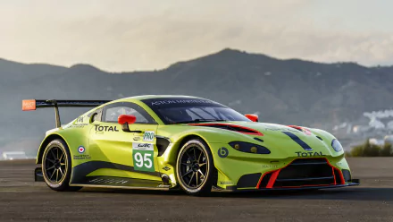 Aston Martin Vantage GTE race car in bright green with racing decals, parked on a racetrack with mountains in the background, captured in 4K Ultra HD quality.