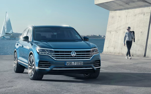 Blue Volkswagen Touareg SUV parked on a waterfront concrete promenade with sailboats and a pedestrian in view — 4K Ultra HD PC desktop wallpaper.