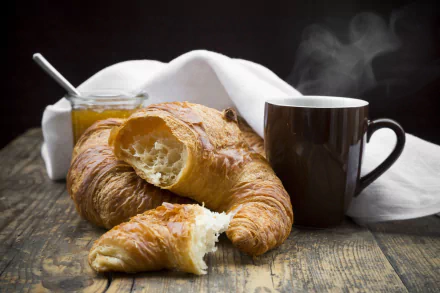 A steaming cup beside flaky croissants and a jar of jam on a rustic wooden table, captured in an HD PC desktop wallpaper showcasing viennoiserie and breakfast food.