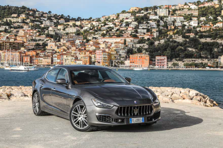 Silver Maserati Ghibli parked by a waterfront with colorful hillside buildings in the background, captured in stunning 4K Ultra HD detail for a PC desktop wallpaper.