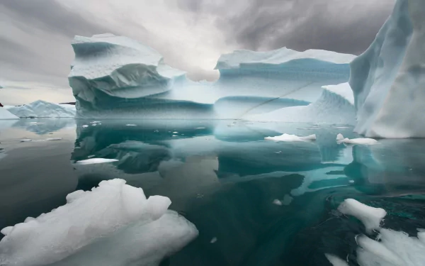 HD desktop wallpaper featuring a serene nature scene of icebergs with crisp reflections on calm water under an overcast sky.