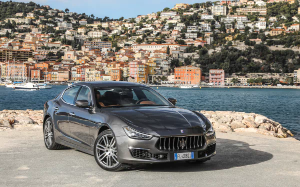 Silver Maserati Ghibli parked by a waterfront with colorful hillside buildings in the background, captured in stunning 4K Ultra HD detail for a PC desktop wallpaper.