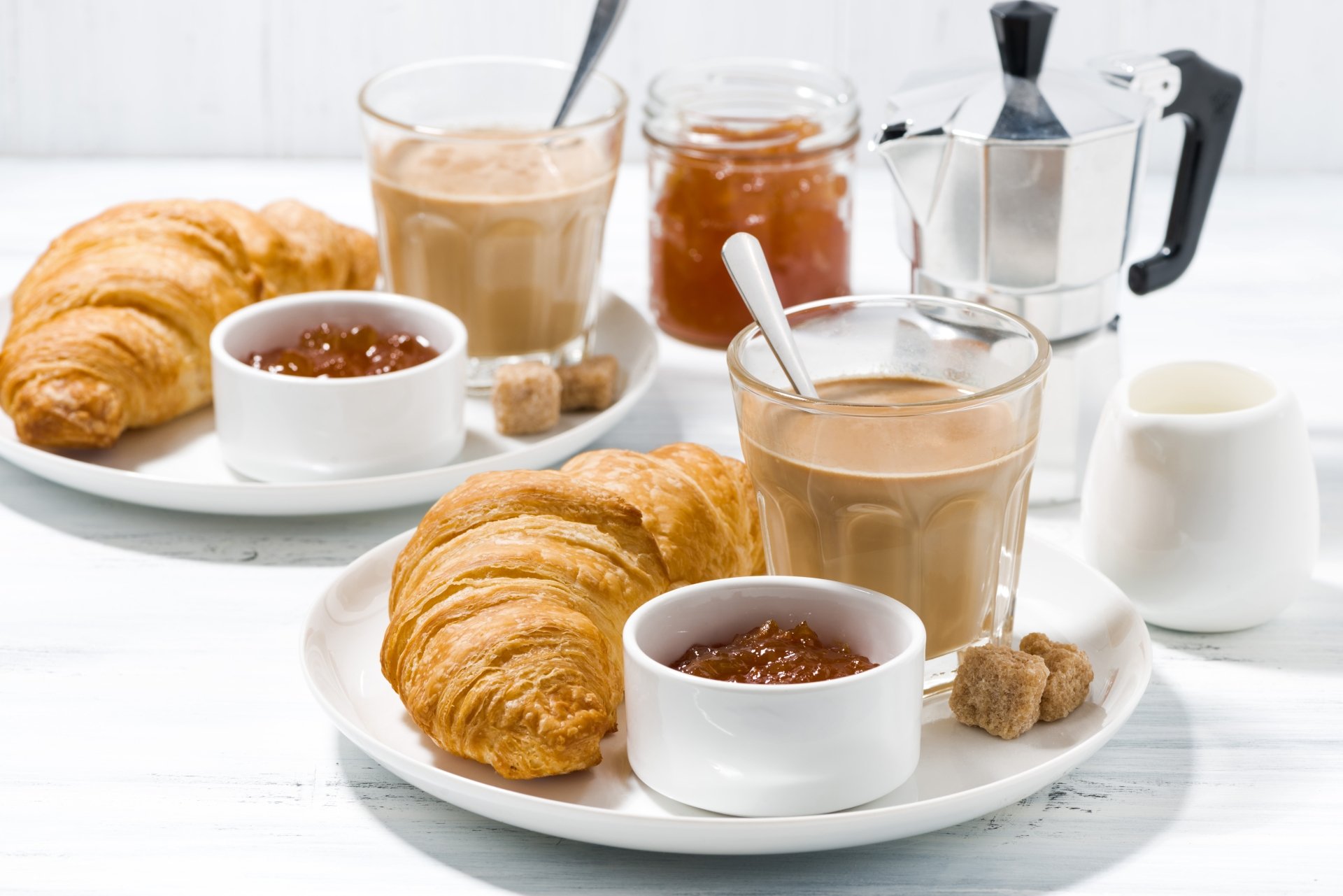 A 4K Ultra HD desktop wallpaper featuring a breakfast scene with golden croissants, a cup of coffee with milk, jars of jam, and a moka pot on a white table.