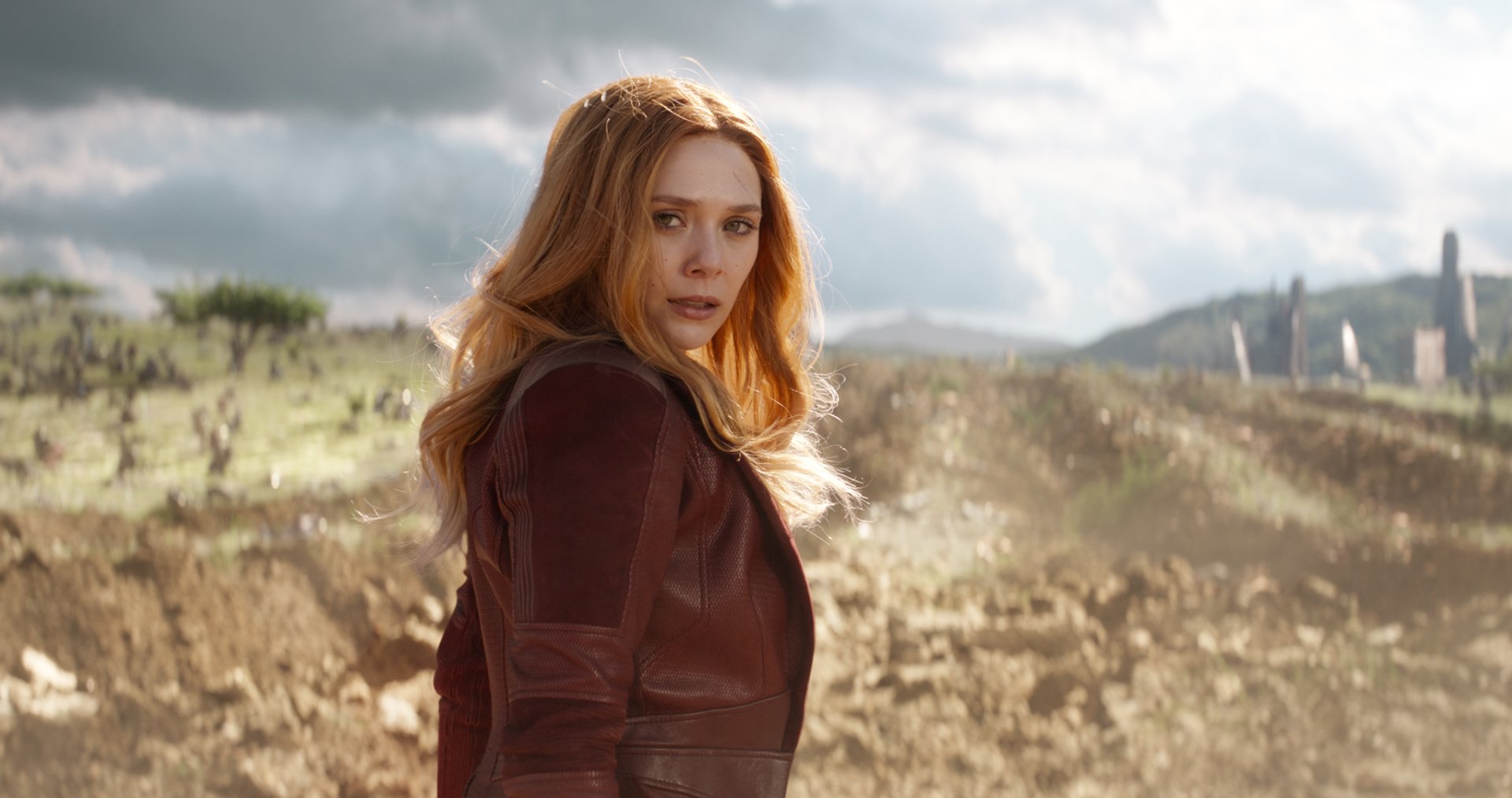 HD desktop wallpaper featuring Elizabeth Olsen as Scarlet Witch in Avengers: Infinity War. She stands in a rugged landscape, looking over her shoulder with a determined expression.