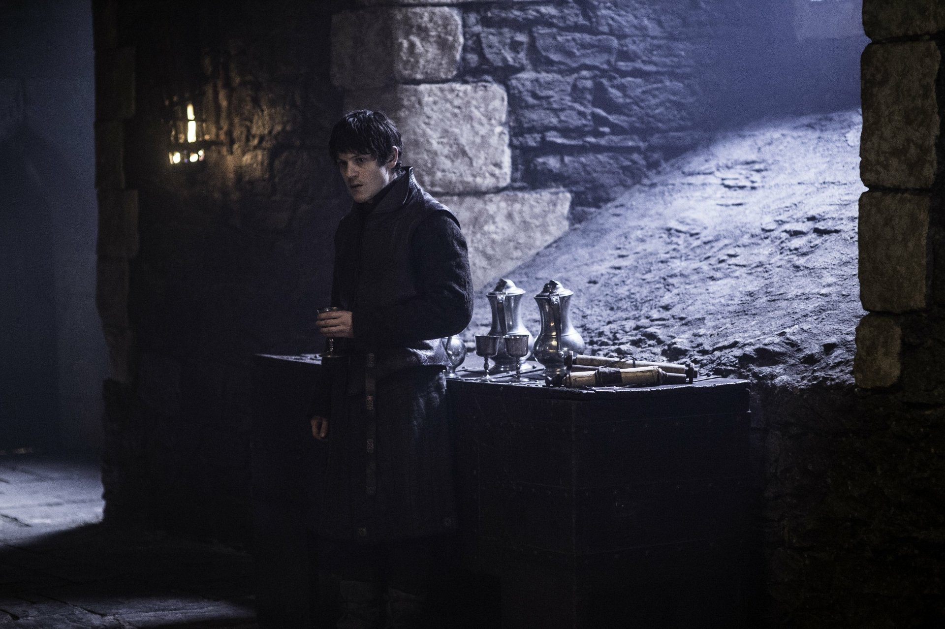 4K Ultra HD PC wallpaper: brooding man in a dim medieval stone chamber evoking Game of Thrones, moody lighting and metal tableware on a wooden chest.