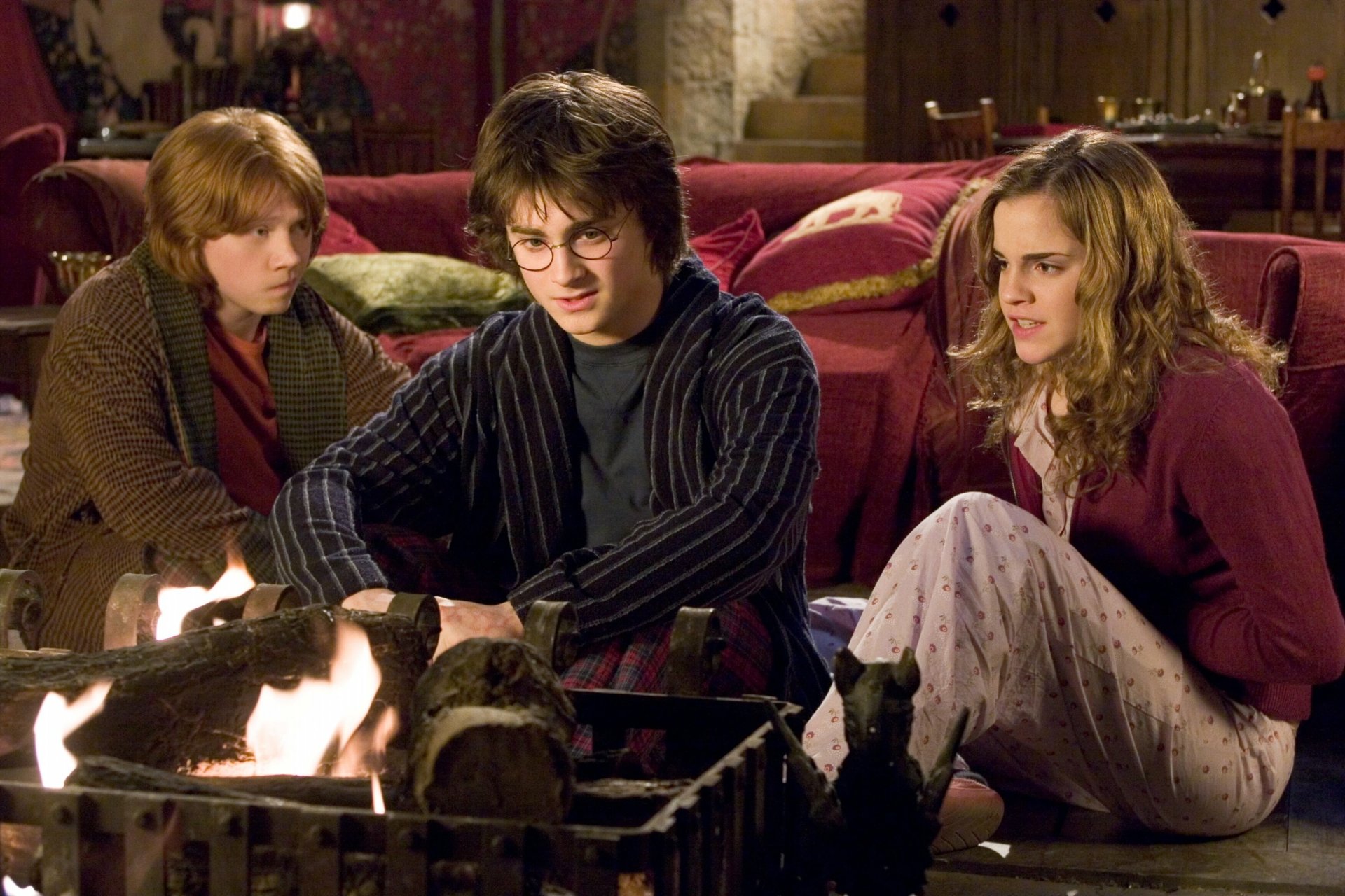 Harry Potter, Ron Weasley, and Hermione Granger, played by Daniel Radcliffe, Rupert Grint, and Emma Watson, gathered around a fire in a scene from Harry Potter and the Goblet of Fire.
