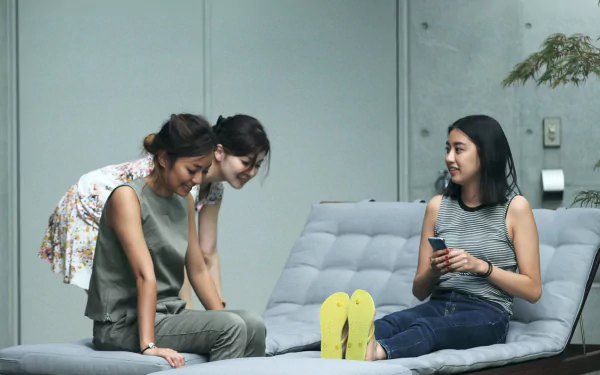 HD desktop wallpaper of three individuals from Terrace House casually conversing on a grey sofa, with a serene, modern background atmosphere.