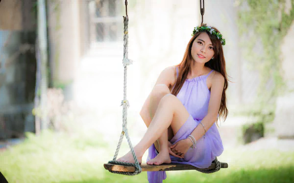 A smiling Asian woman with long brunette hair wearing a purple dress sits gracefully on a swing, captured with a soft depth of field in a 4K Ultra HD wallpaper.
