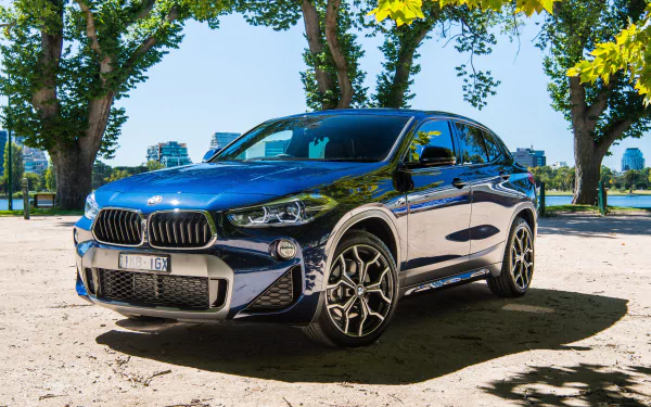 A sleek black BMW X2 SUV parked under leafy trees, captured in stunning 4K Ultra HD as a vibrant PC desktop wallpaper and background.