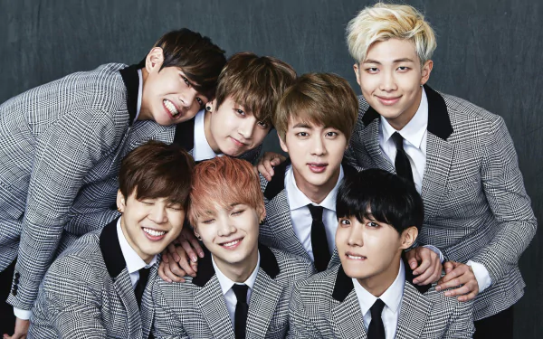 HD desktop wallpaper and background image featuring the music group BTS, showing all seven members dressed in matching grey checkered suits and ties, smiling and posing closely together.