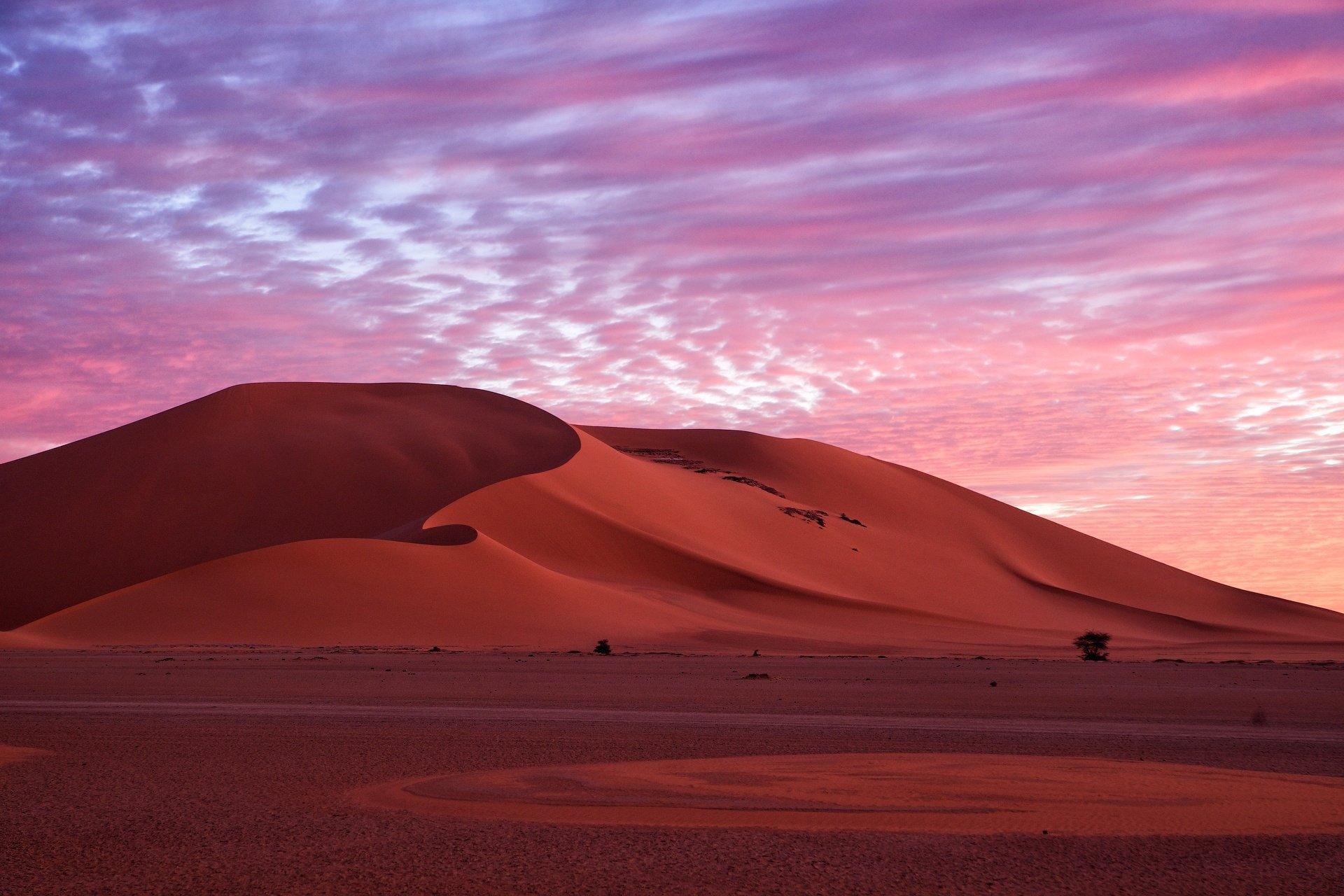 HD desktop wallpaper showcasing a vast desert landscape with smooth sand dunes under a vibrant purple and pink sky at sunset.