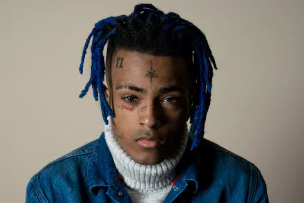 HD desktop wallpaper featuring XXXTentacion with blue dreadlocks and distinctive facial tattoos, set against a plain background.