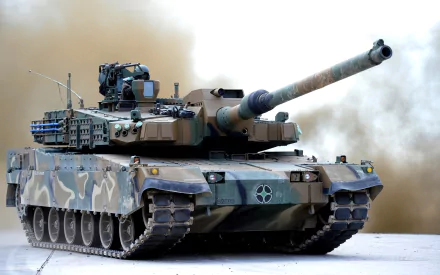 HD desktop wallpaper featuring a K2 Black Panther tank in military camouflage, positioned with its main gun aimed forward against a smoky background.